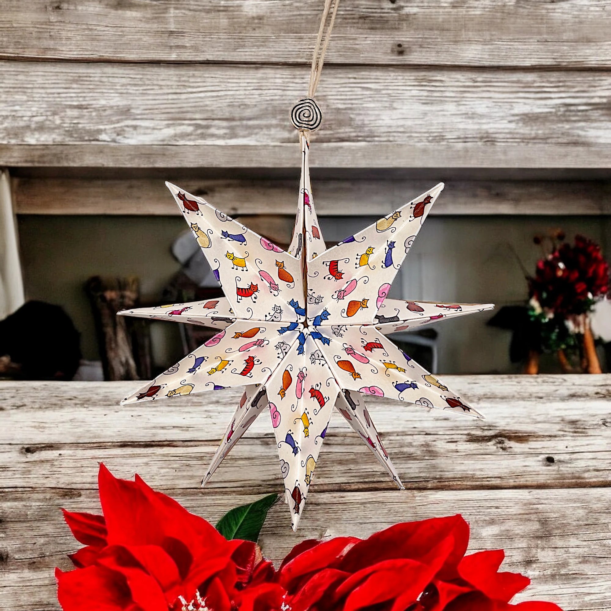 Papierstern mit Comic-Katzen vor einer Holzwand mit rote Blume