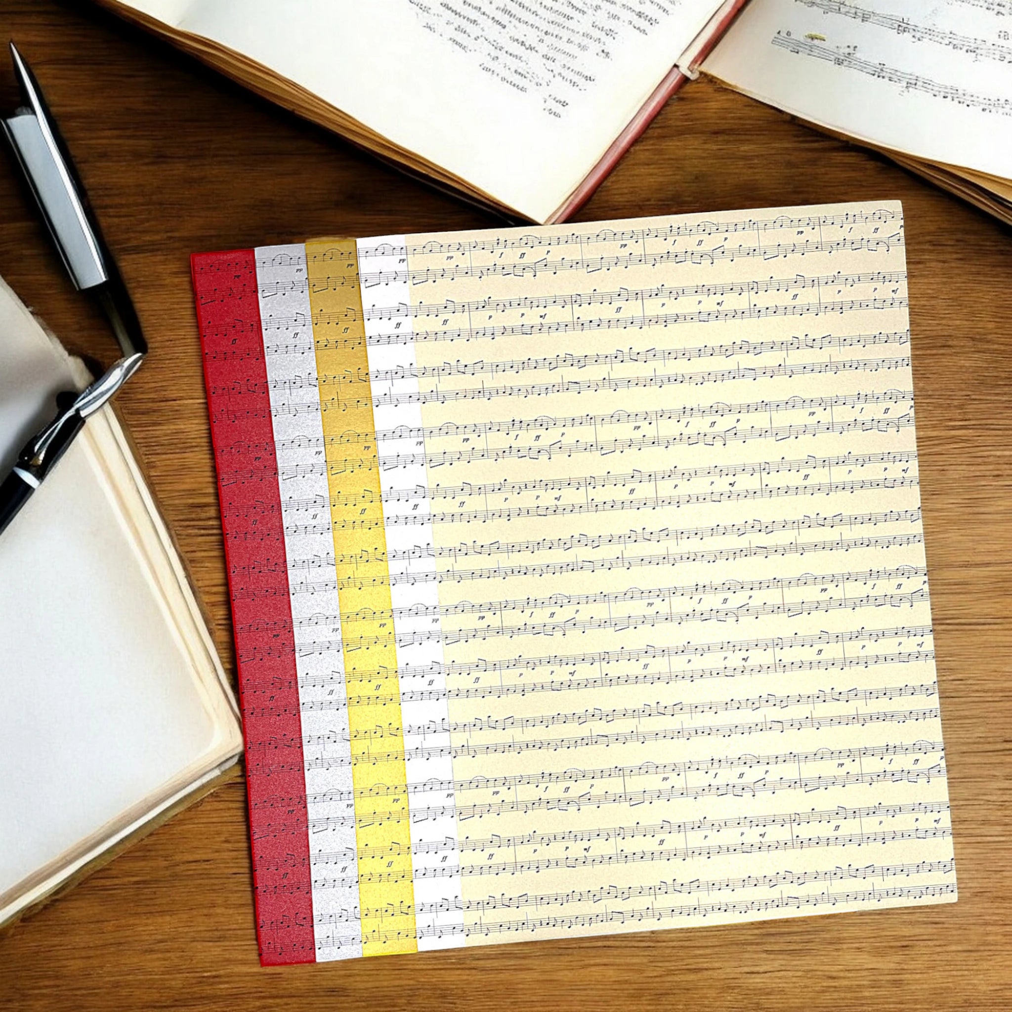 Notenpapier aus Perlglanzpapier in fünf Farben – auf Holztisch mit Stift und Block