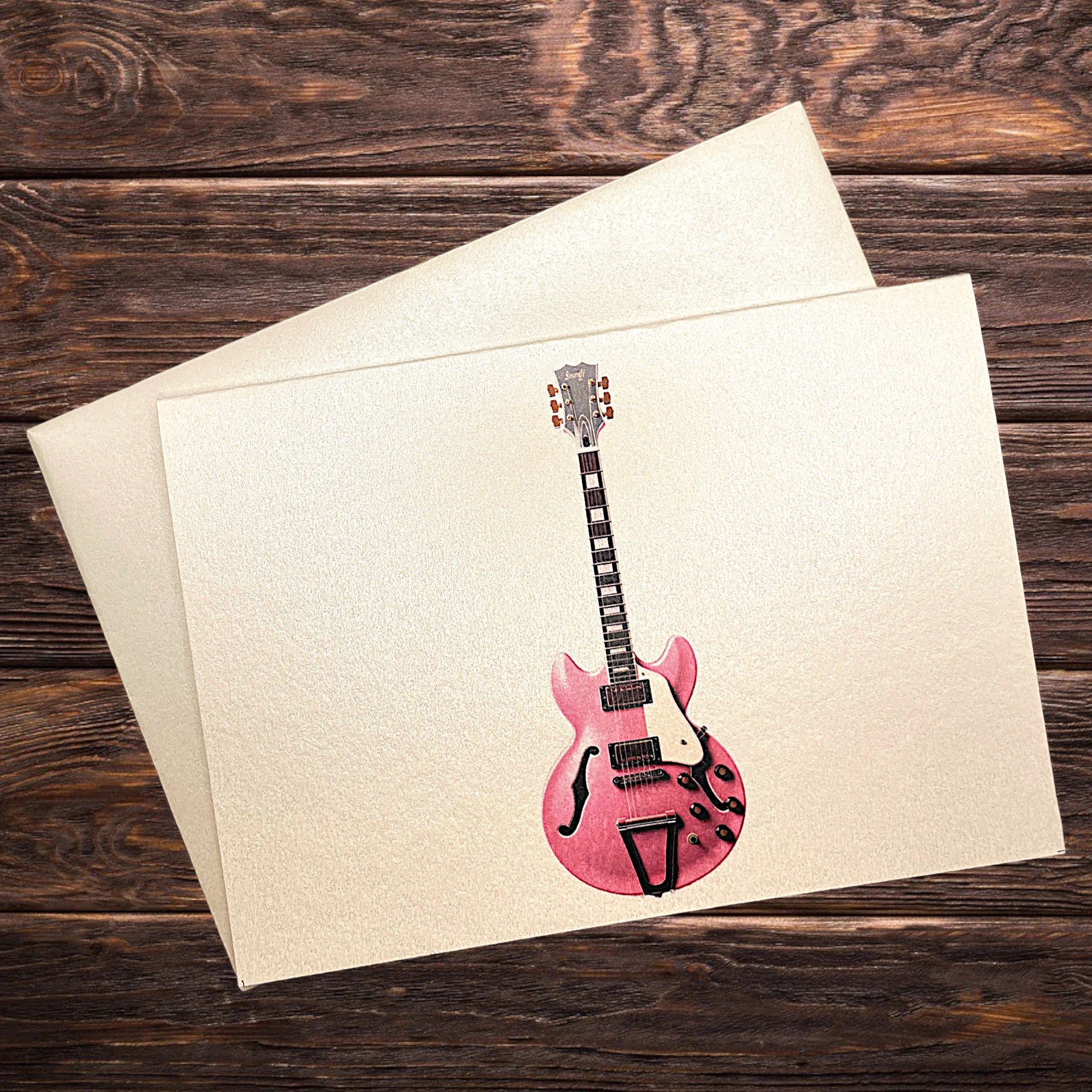 Musik-Klappkarte mit rosa E-Gitarre, präsentiert auf rustikalem Holztisch