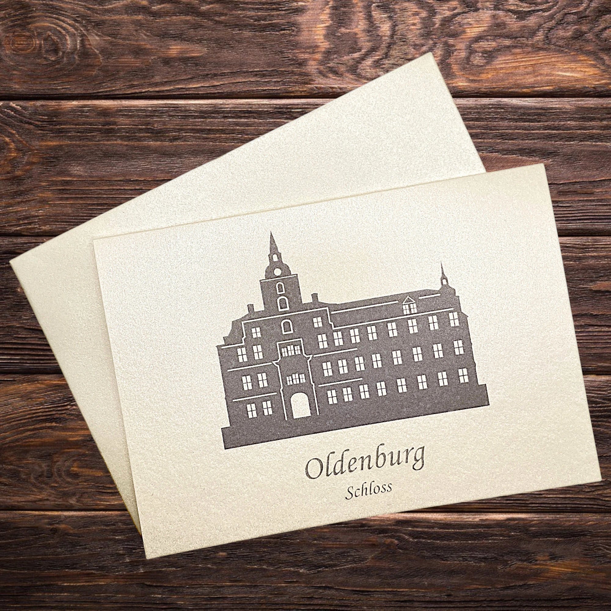 Klappkarte mit dem Oldenburger Schloss in Grau – elegant inszeniert auf dunkler, rustikaler Tischwand