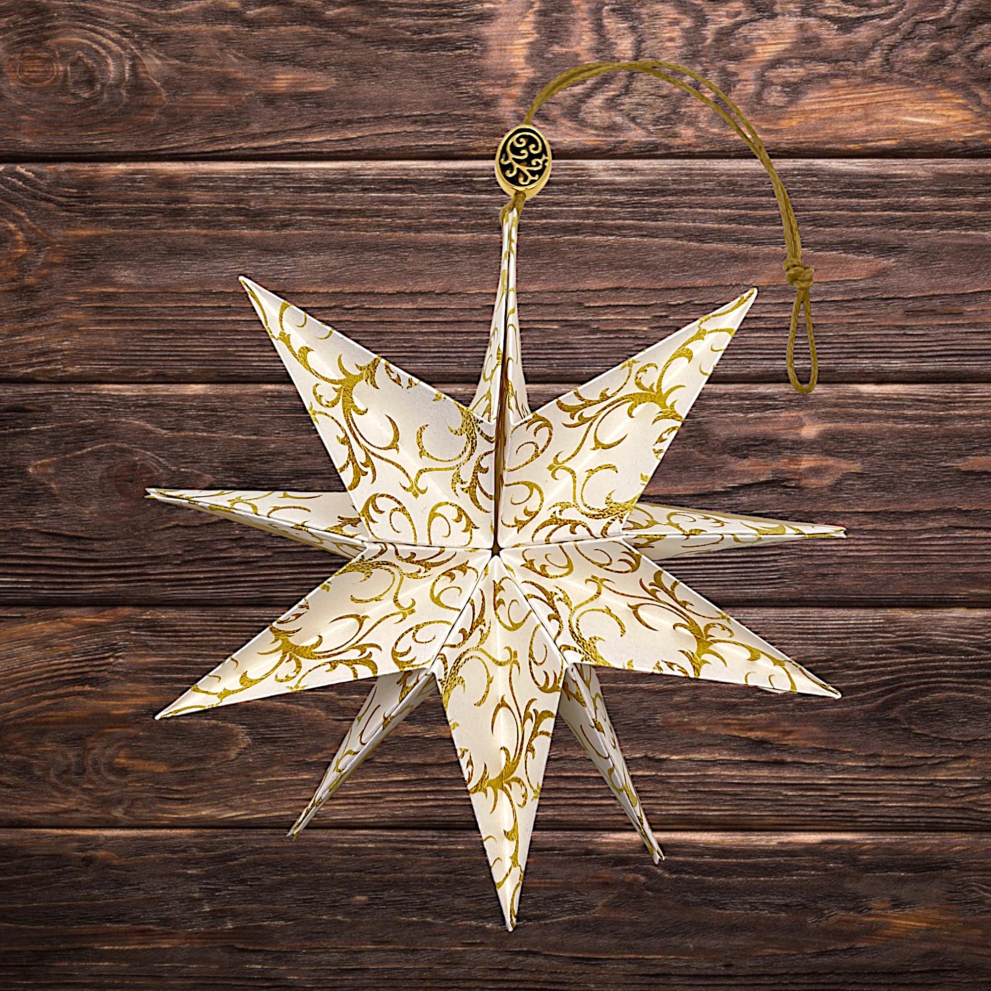Papierstern Arabeske Gold-weiß, aufgeklappt vor Holzwand.