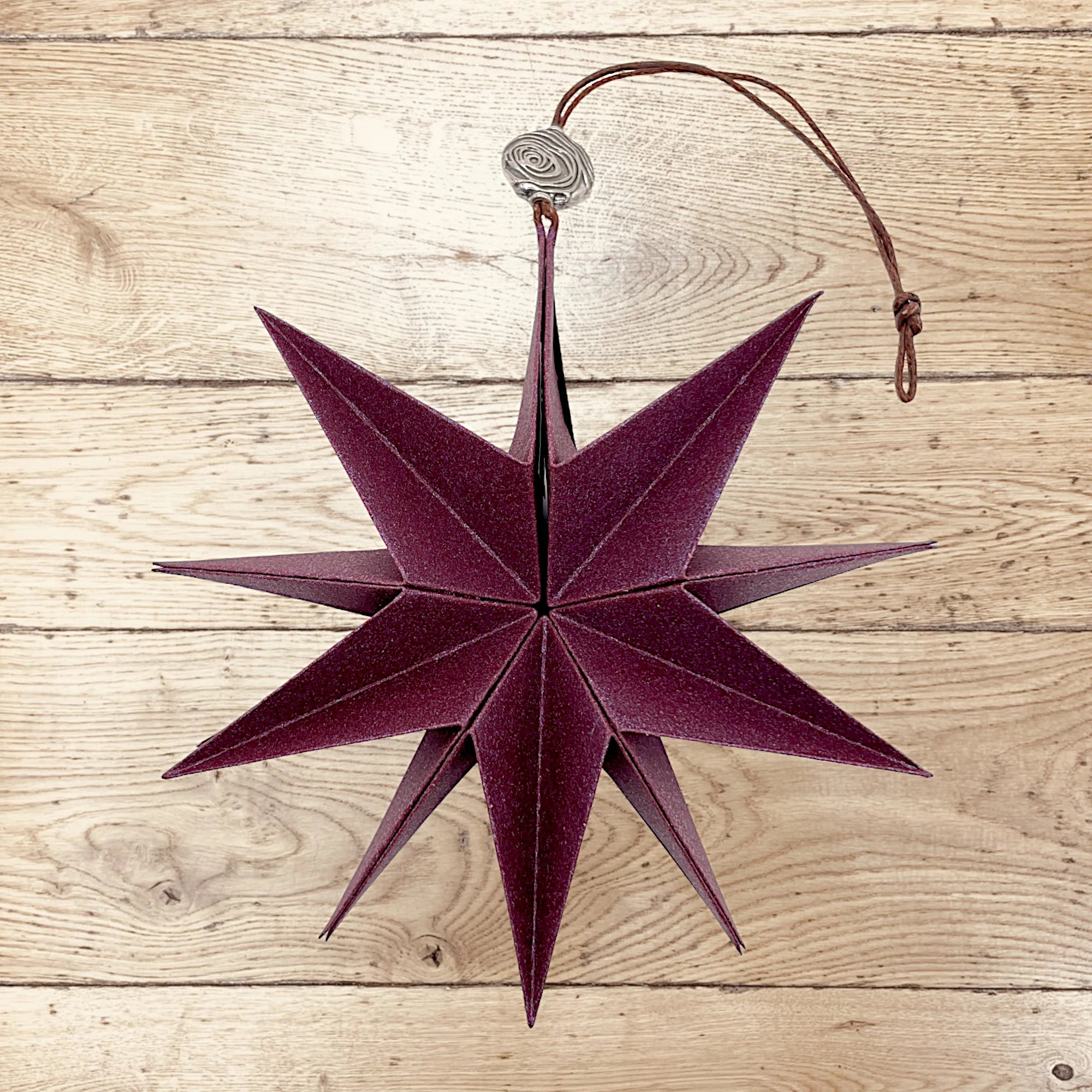 Dunkelroter Papierstern in Bordeaux, stilvoll arrangiert auf rustikalem Holztisch