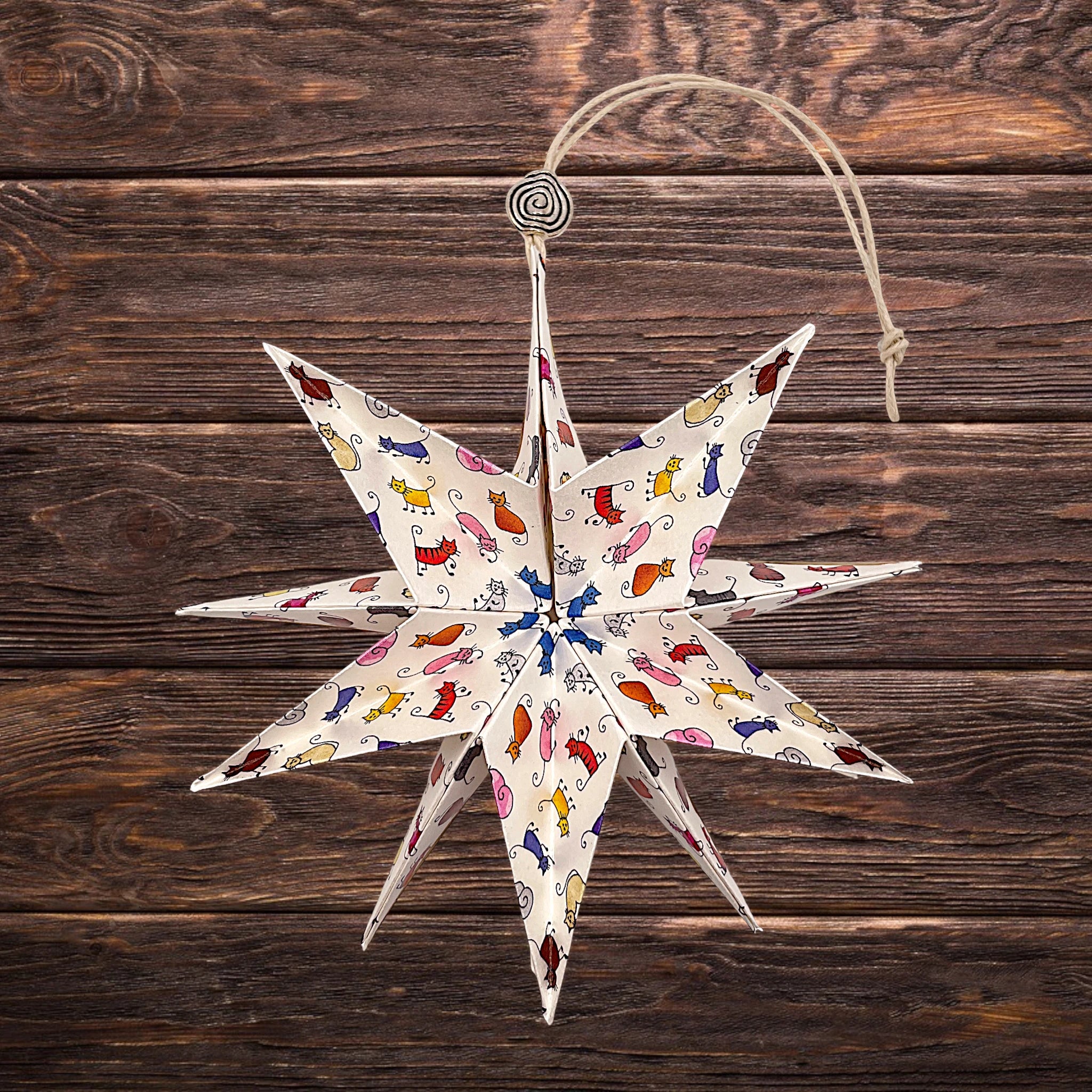 Papierstern mit bunten Comic-Katzen, dekorativ auf rustikalem Holztisch arrangiert