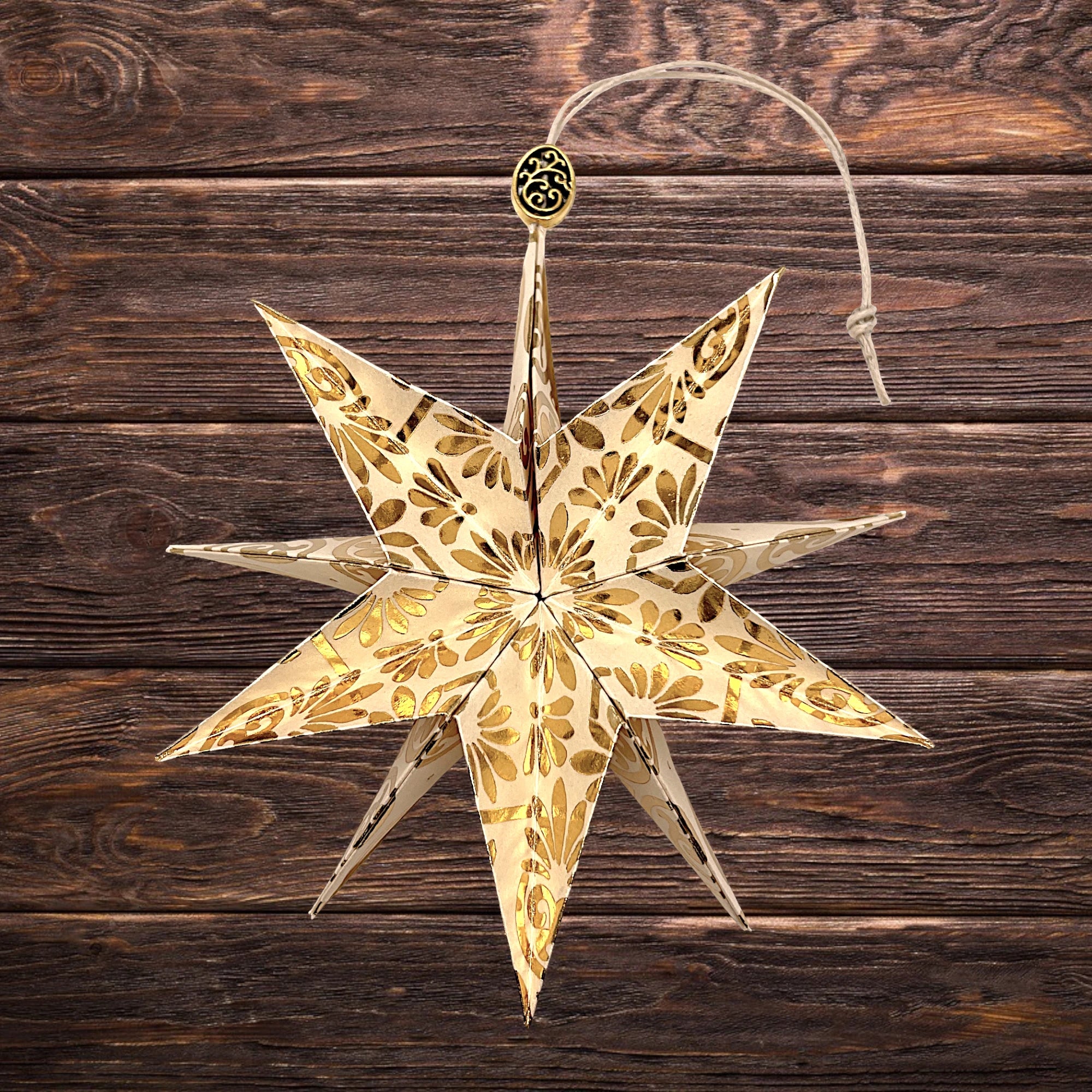 Cremefarbener Papierstern mit goldglänzendem Muster, festlich auf Holztisch arrangiert