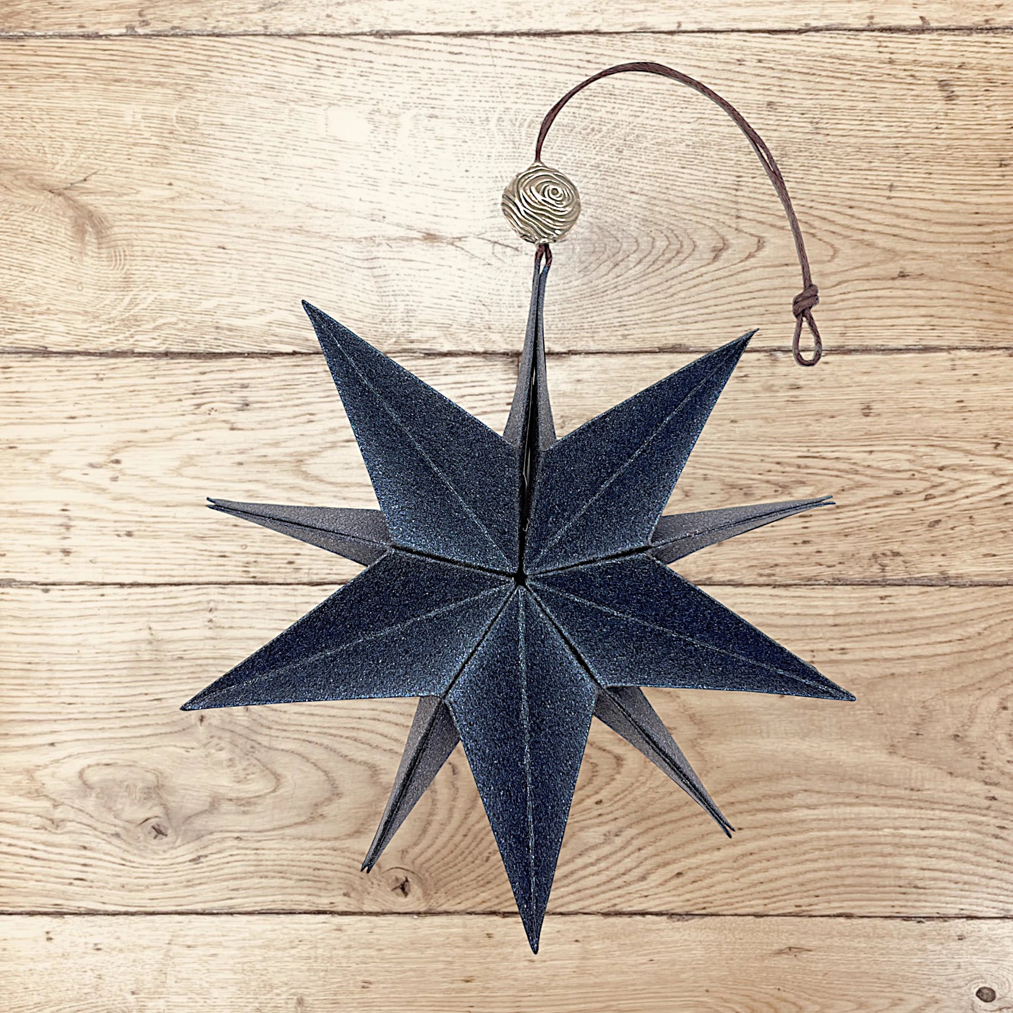 Dunkelblauer Papierstern aus schimmerndem Perlglanzpapier, dekorativ auf Holz präsentiert