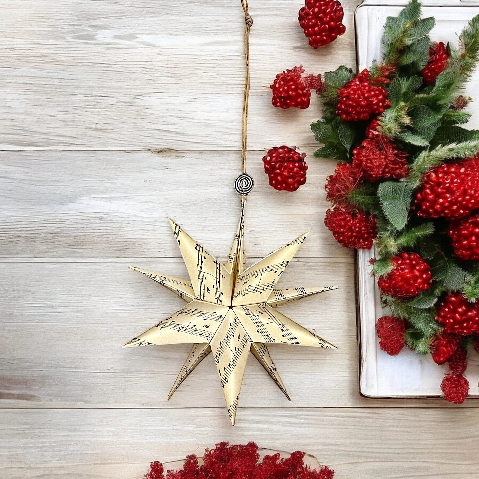 Papierstern mit Notenmuster, hängend vor heller Holzwand mit roten Beeren und grünen Zweigen