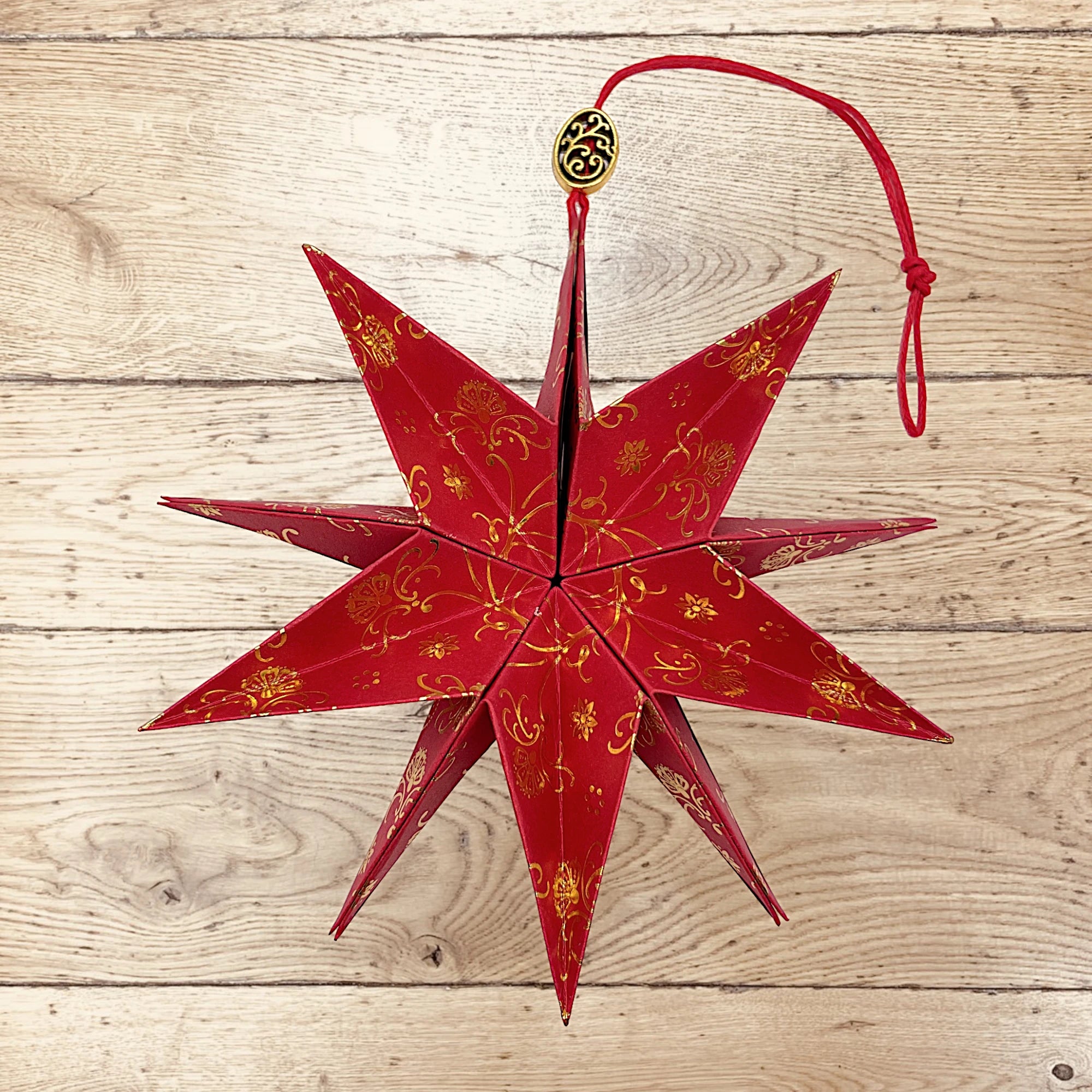 Roter Papierstern mit glänzendem Golddruck, festlich dekoriert auf rustikalem Holztisch