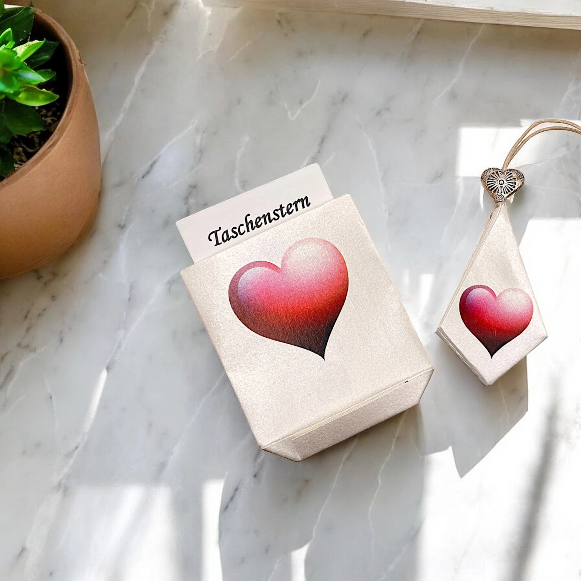 Geschlossener Papierstern mit rotem Herz und Etui, arrangiert auf Marmortisch