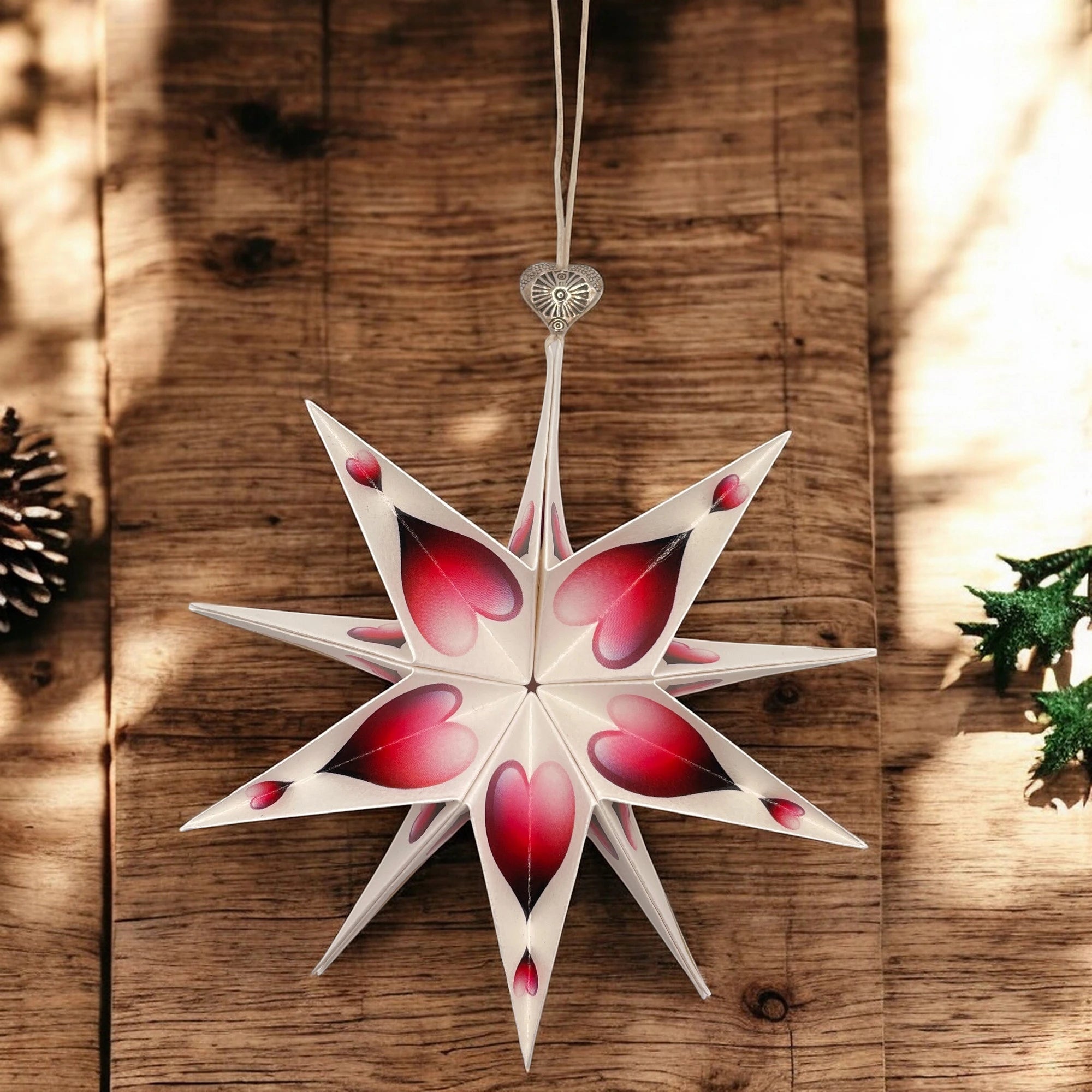 Papierstern mit rotem Herzmotiv, schattig hängend vor rustikaler Holzwand