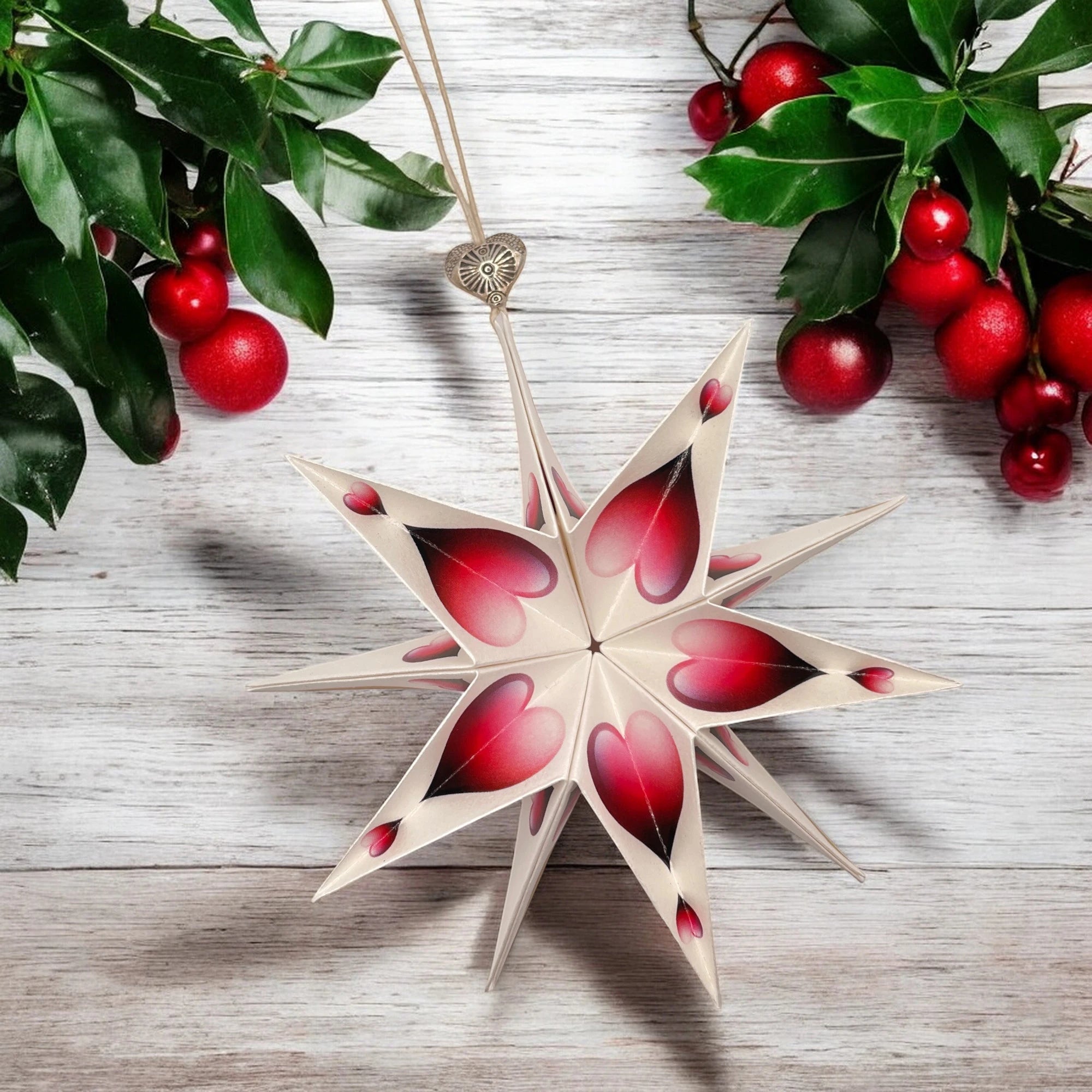 Papierstern mit rotem Herzmotiv auf hellem Tisch, dekoriert mit Ilex und roten Beeren