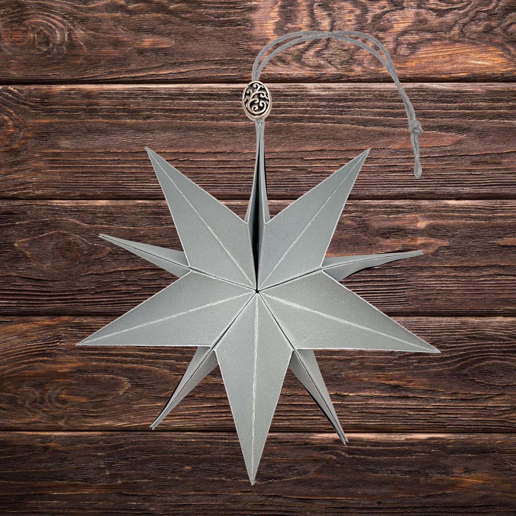 Dekorativer Stern aus silberfarbenem Perlglanzpapier, edel inszeniert auf Holz
