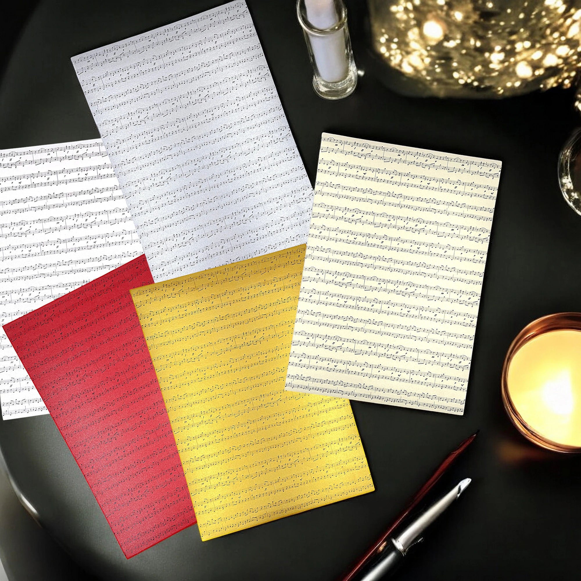 Set aus fünf Farben Papier mit Notendruck – dekorativ auf Holztisch mit Stift und Kerze