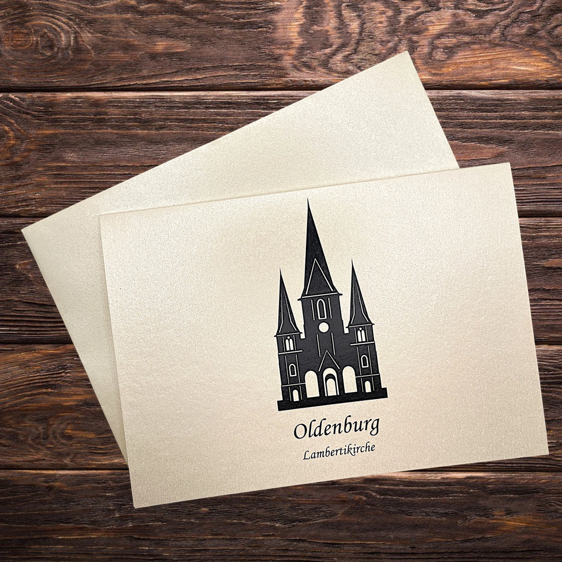 Auf einem Holztisch eine Karte mit Umschlag. Motiv die Lambertikirche aus Oldenburg