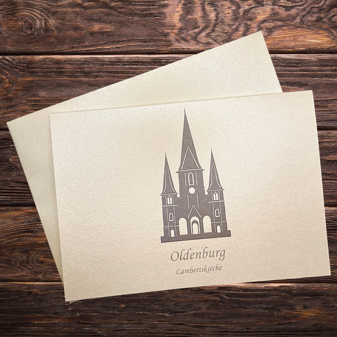 Auf einem Holztisch eine Klappkarte mit der Lambertikirche in grau