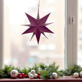 Hängender papierstern vor einem Fenster zu Weihnachten